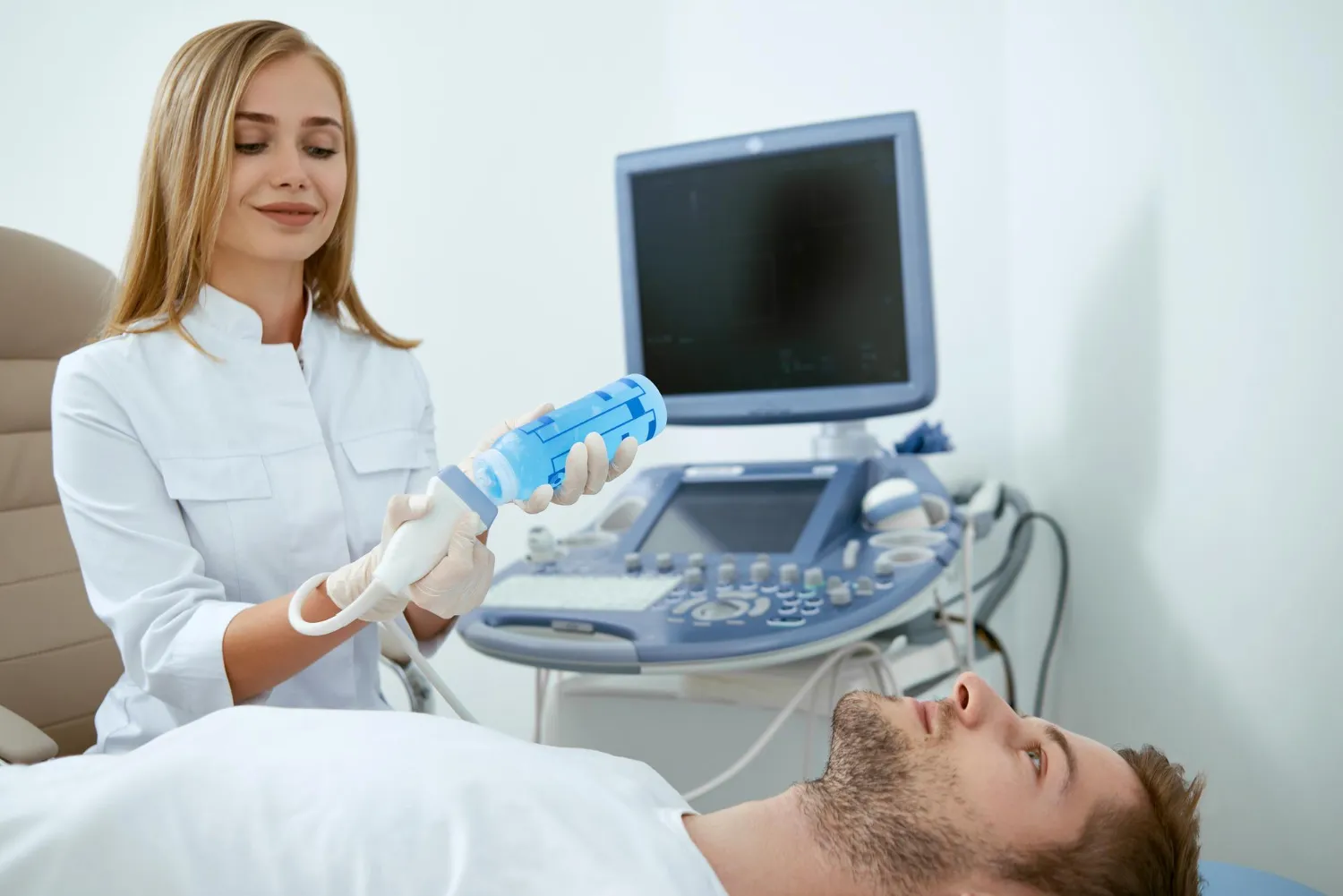 Médico sosteniendo un dispositivo de ultrasonido mientras atiende a un paciente en una consulta médica, con un equipo de diagnóstico al fondo.